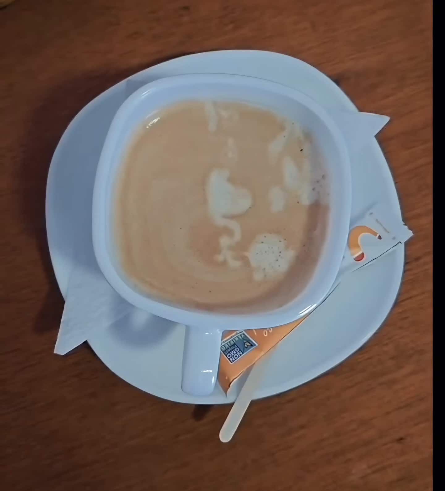 Capuchino visto desde arriba en taza y plato blancos sobre una mesa de madera