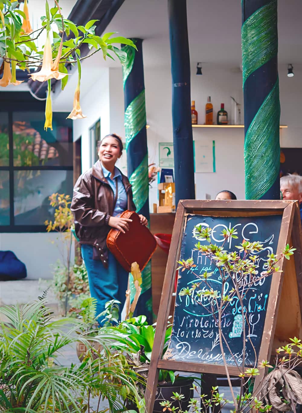 Visitante sonriente con chaqueta de cuero junto a columnas verdes y un tablero de café escrito con tiza