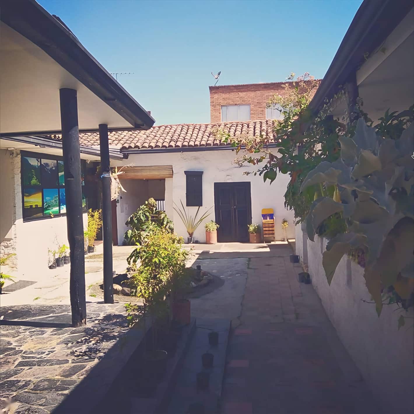Pasillo soleado del patio con techo de teja, plantas y puertas negras al fondo