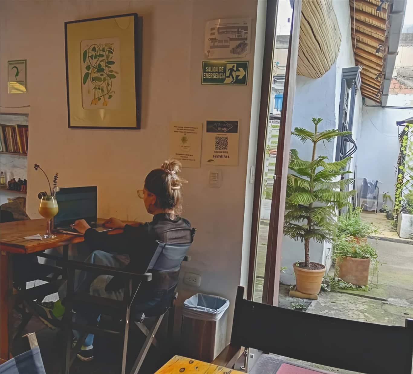 Mujer trabaja en su portátil en una mesa de madera junto a la puerta abierta al patio con plantas