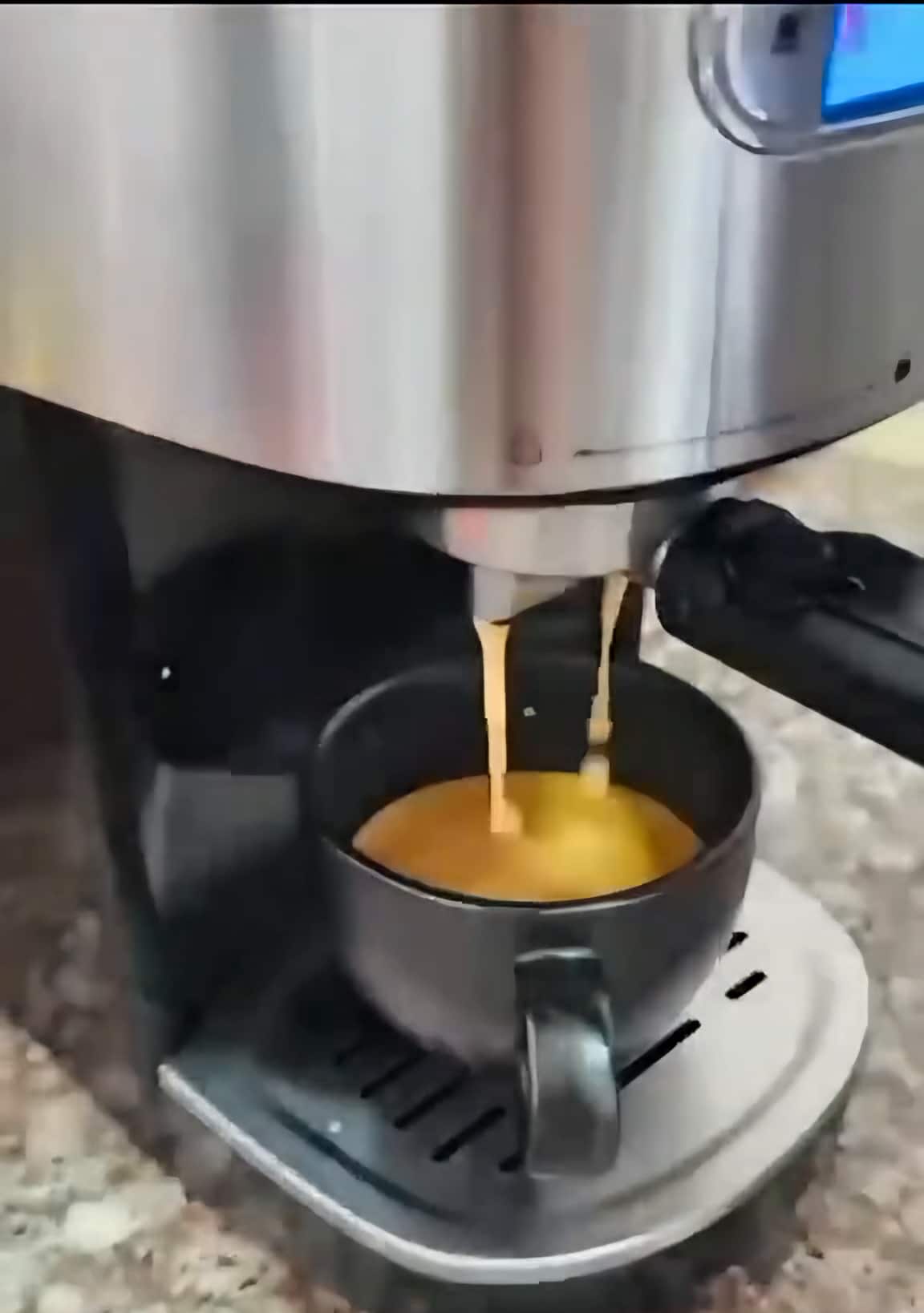 Una cafetera espresso sirve café en una taza negra sobre un mesón de granito