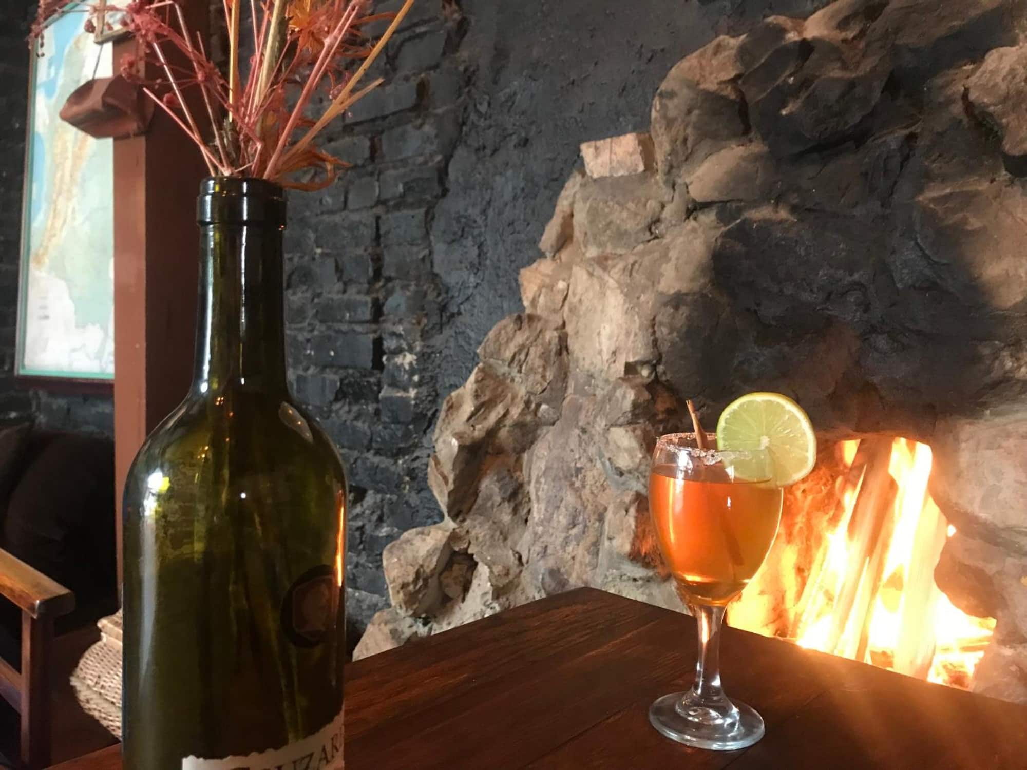 Botella de vino y cóctel frente a la chimenea de piedra