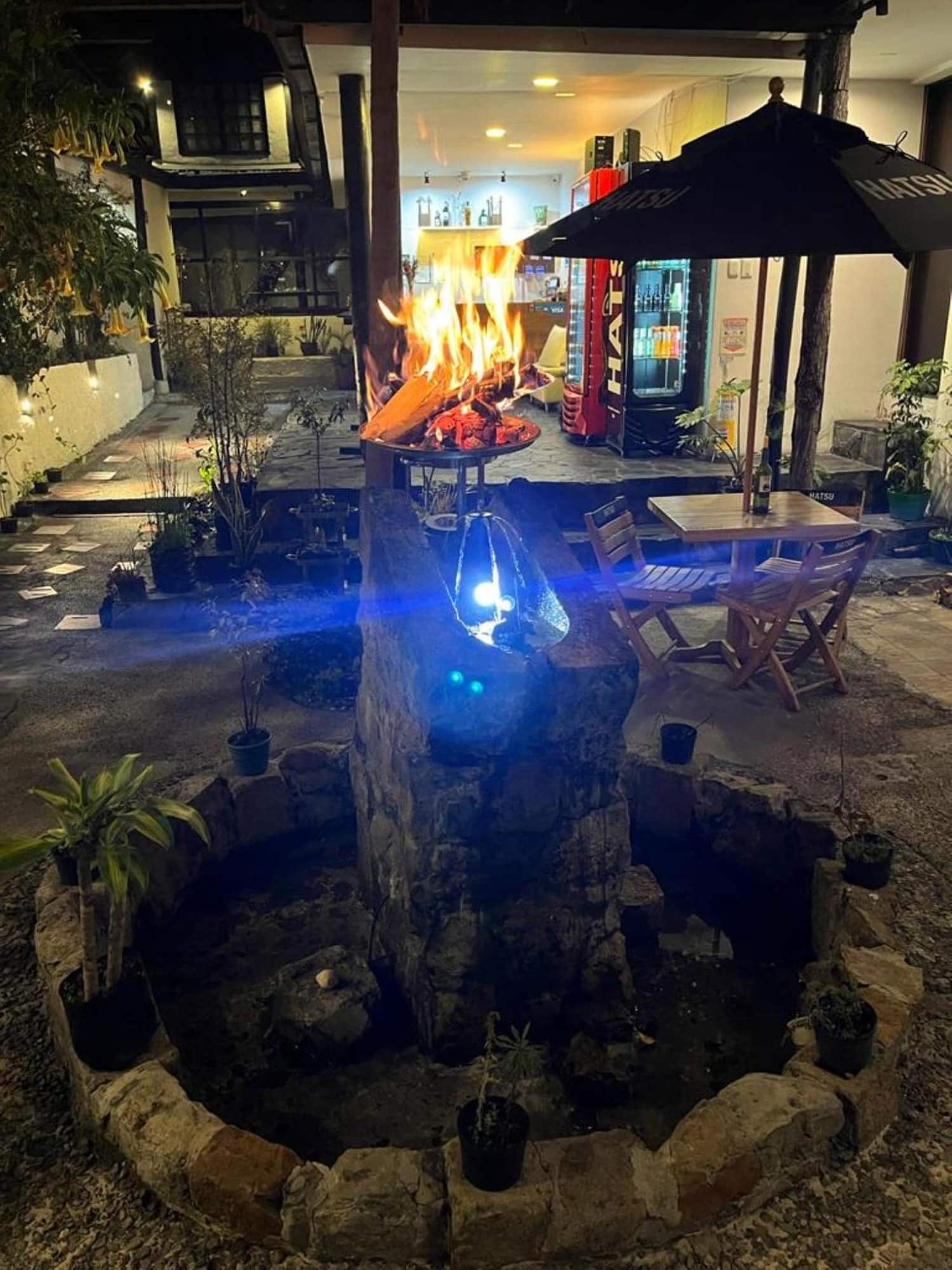 Patio de noche con fogata, estanque de piedra y sombrillas