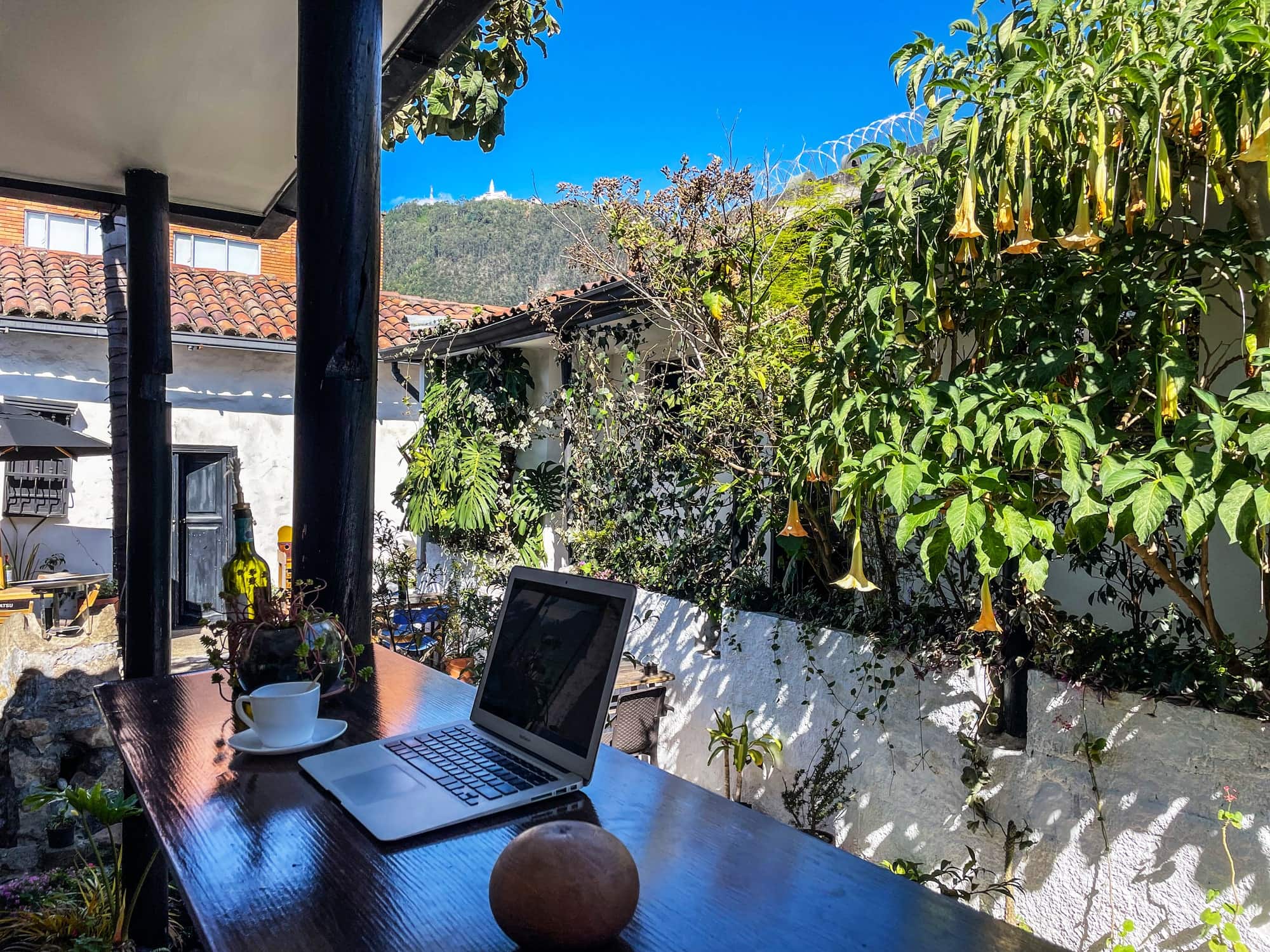 Portátil y café en una mesa de madera, con Monserrate al fondo