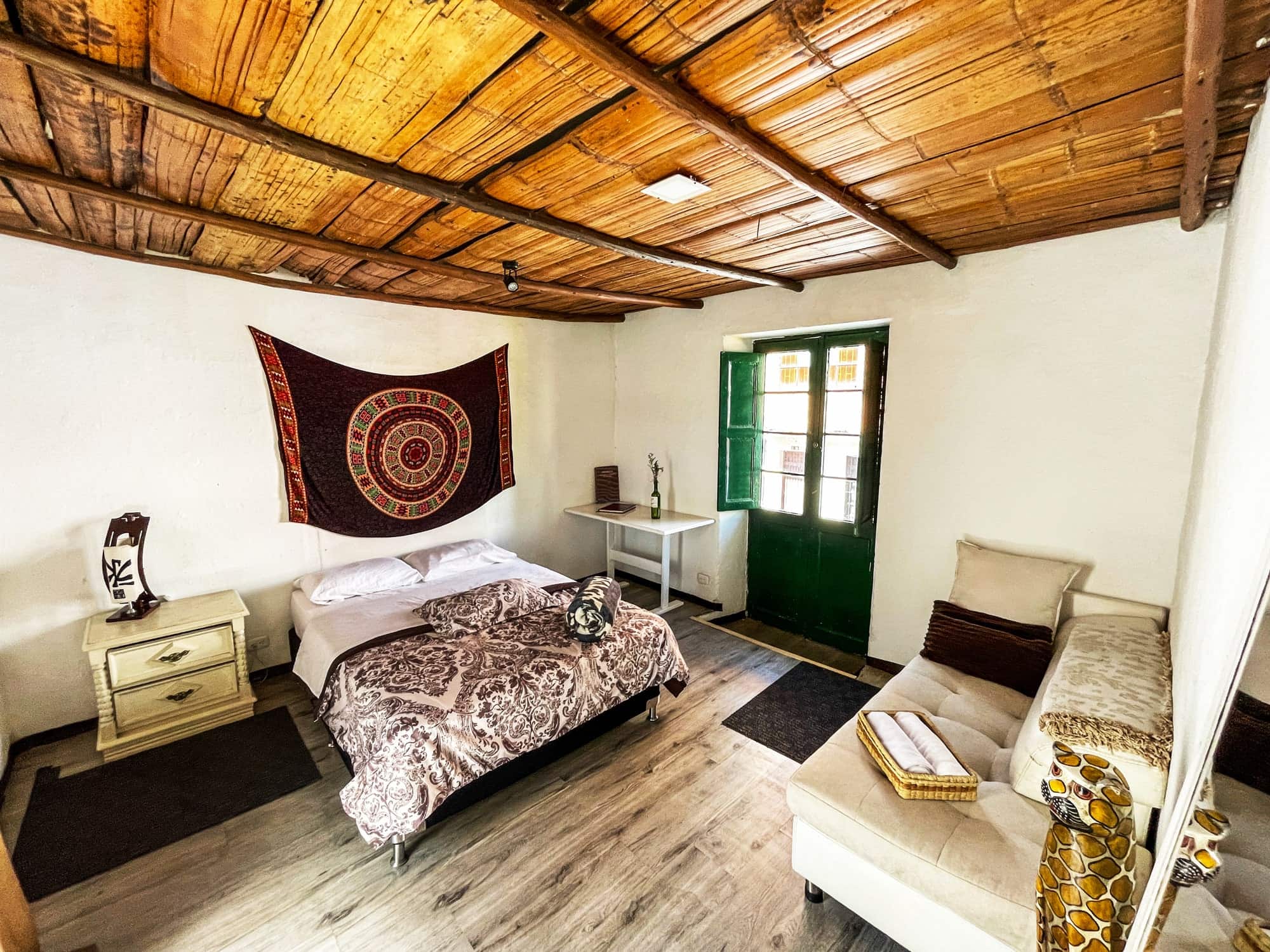 Habitación doble con cama doble, sofá blanco y puerta verde de vidrio