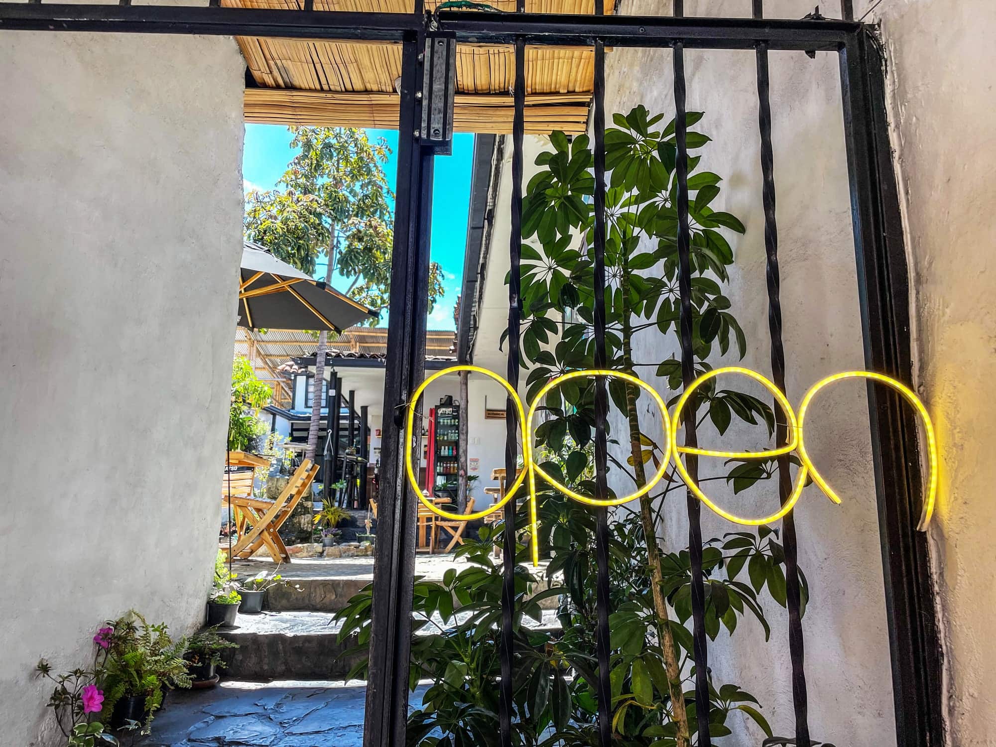 Entrada por reja negra con aviso de neón "open" y plantas