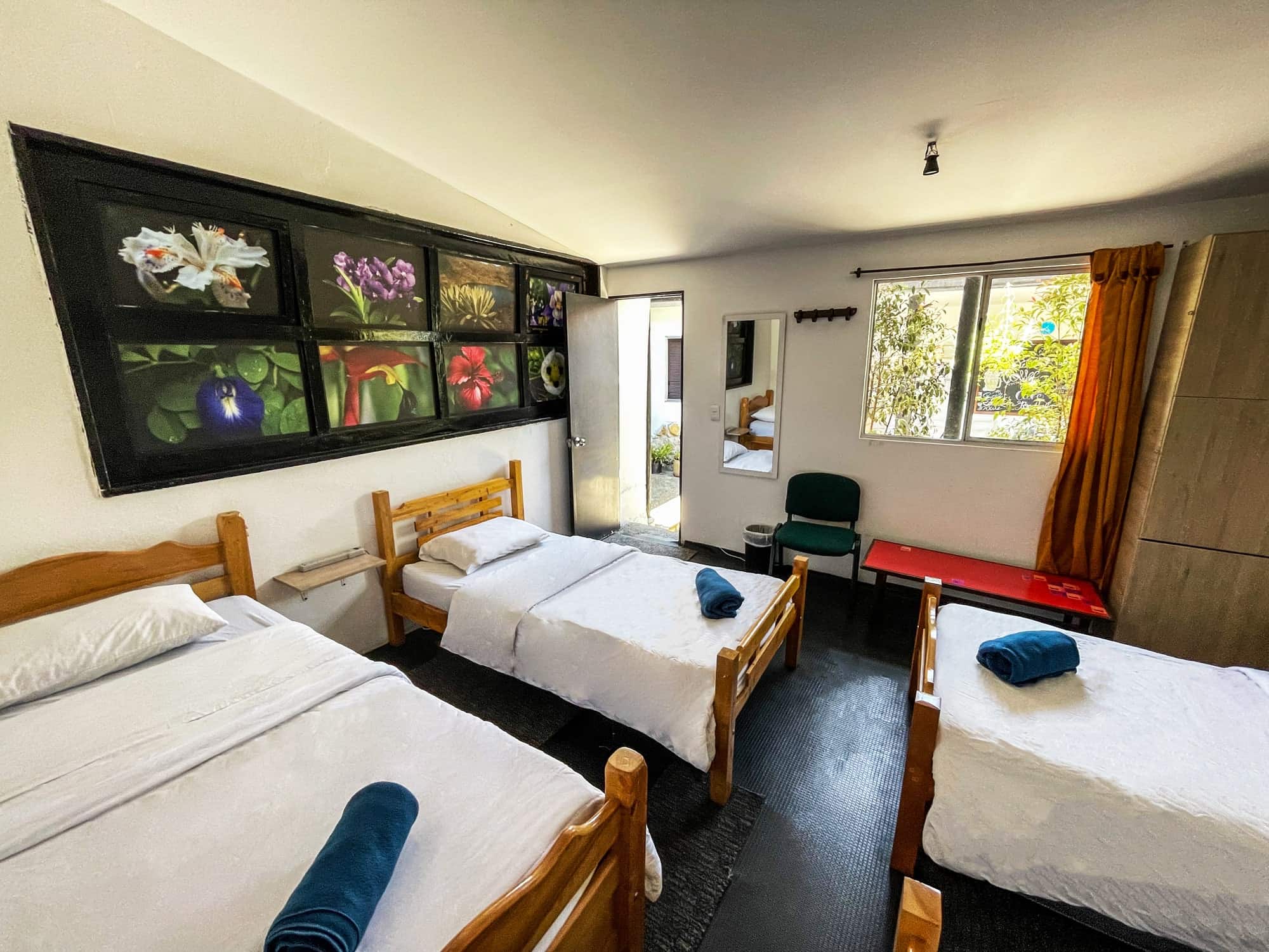 Habitación con tres camas sencillas de madera y cuadros de flores