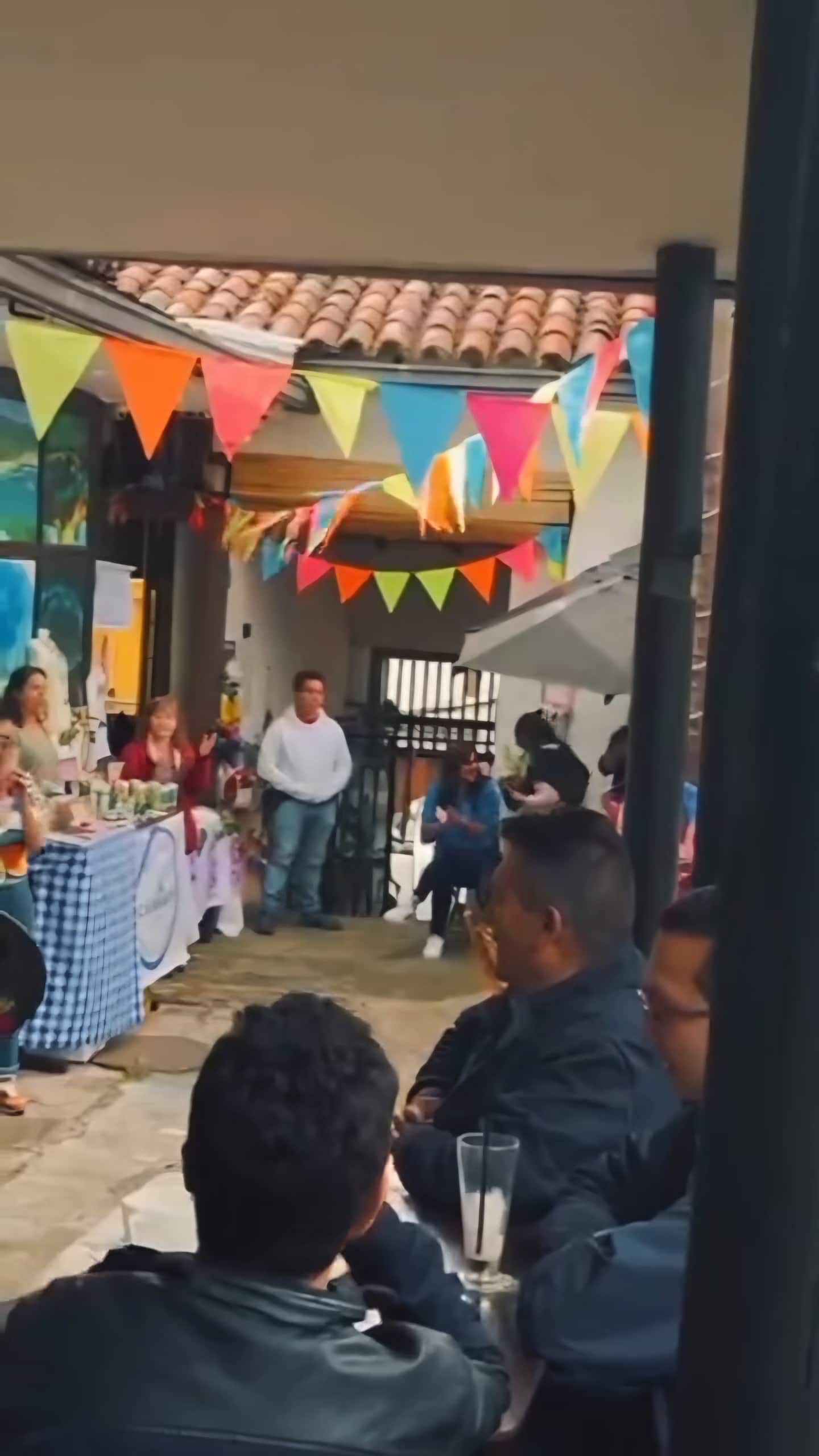 Banderines de colores sobre el corredor del patio durante un evento con mesas y asistentes