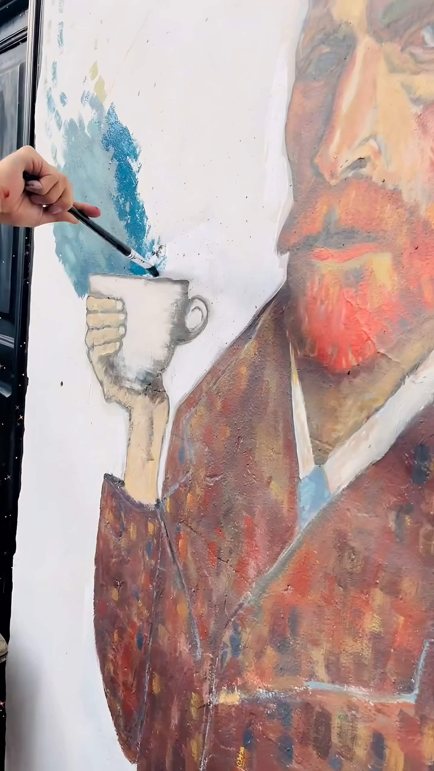 Mano del artista con pincel pinta el remolino azul sobre la taza del mural de Van Gogh