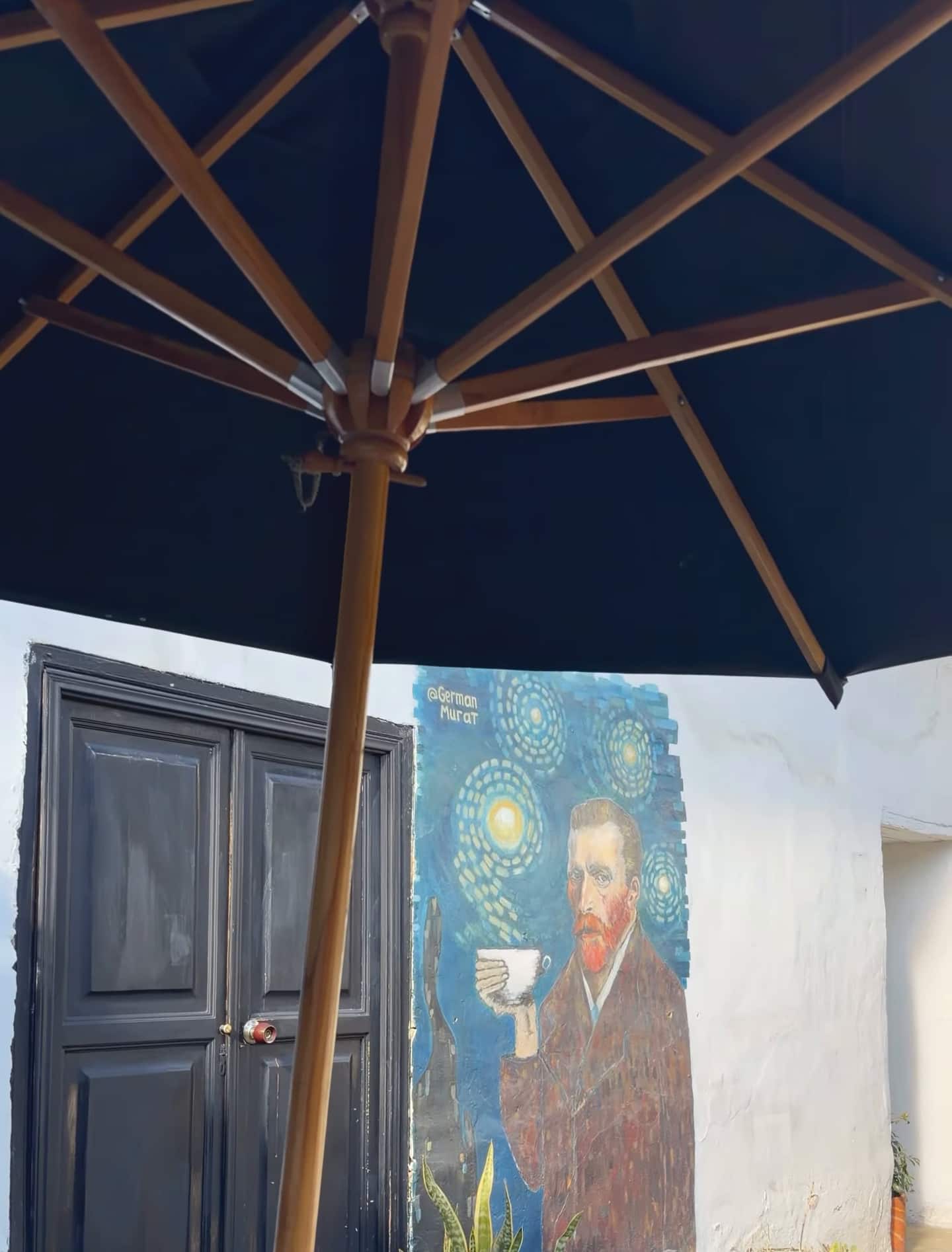 Bajo una sombrilla oscura, el mural de Van Gogh con taza junto a una puerta negra del patio