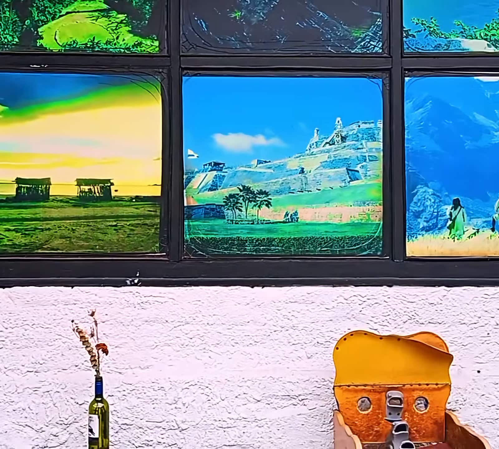 Ventanales con afiches de paisajes colombianos sobre un muro blanco con una botella decorativa